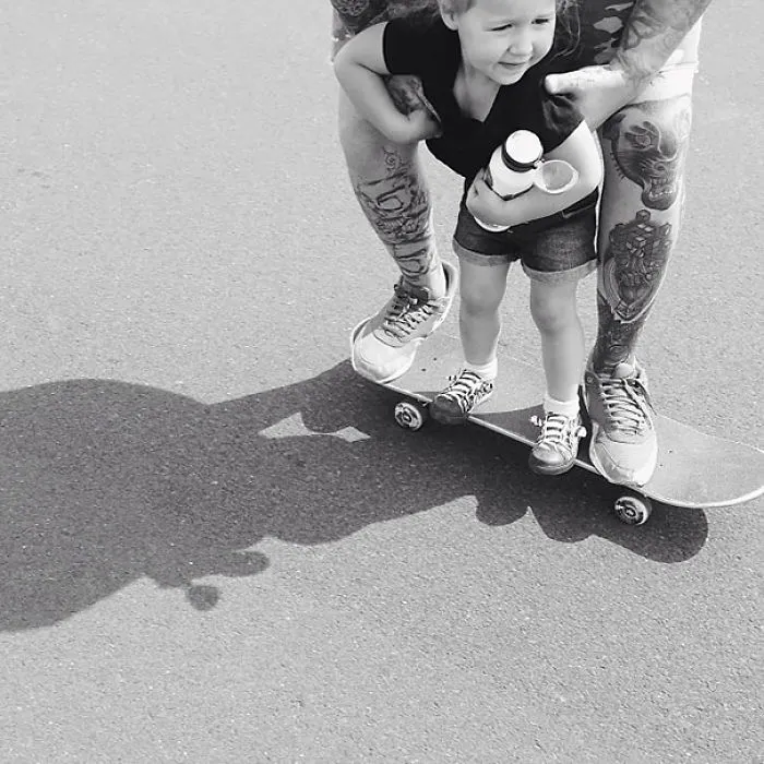 Tattooed parent skateboarding with a smiling baby, showcasing a beautiful connection.