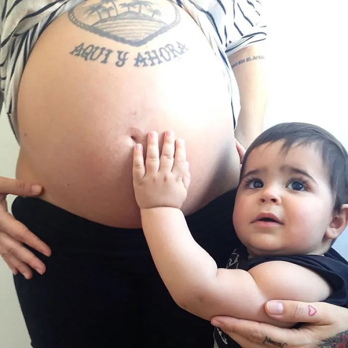 Baby touching tattooed belly, connecting with parent.