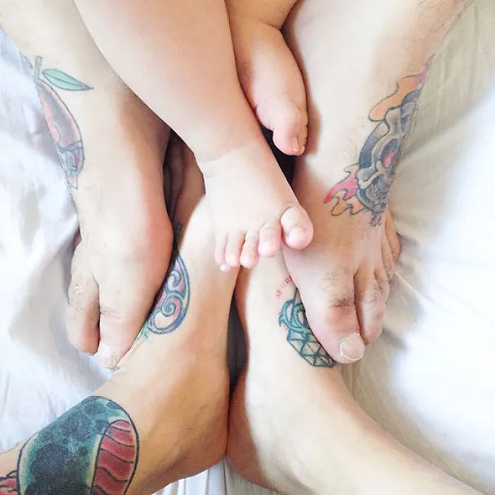 Tattooed parents and their baby touching feet together, showcasing beautiful body art.