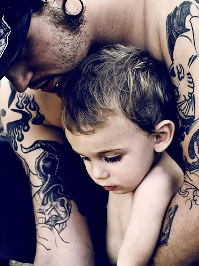 Tattooed parent lovingly embraces their baby, highlighting beautiful family bond.