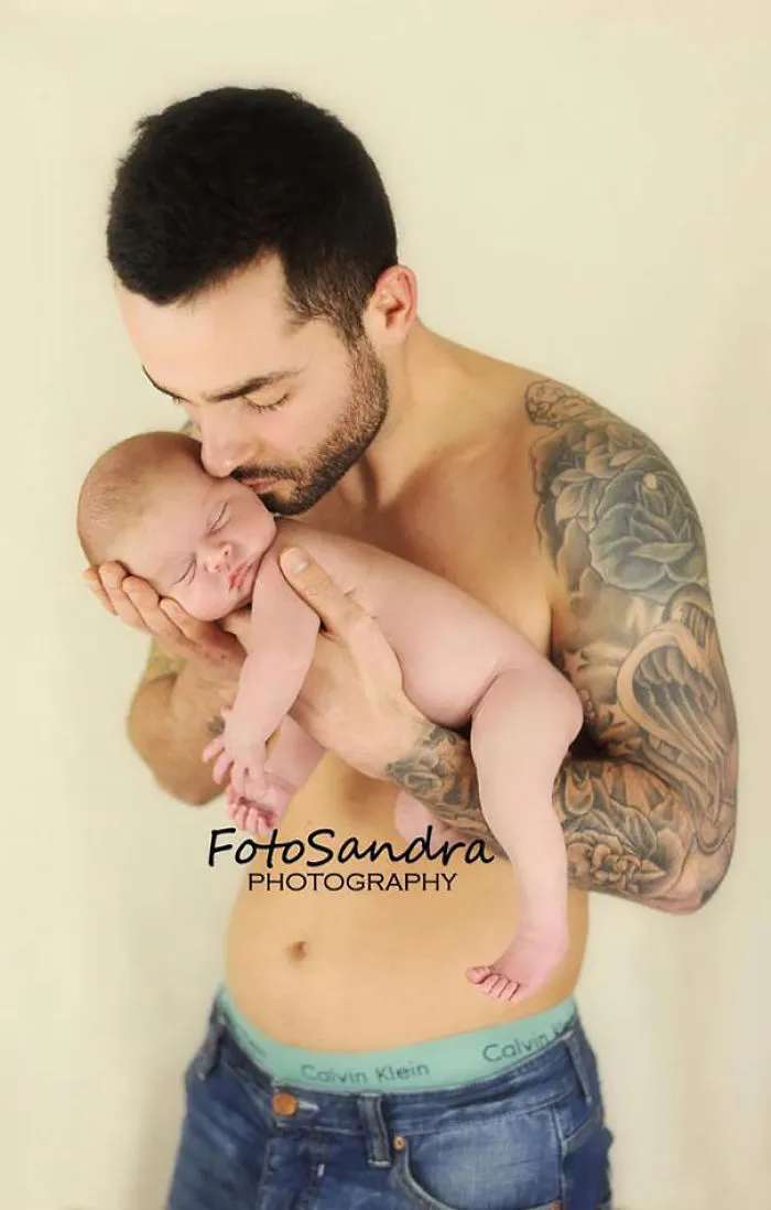 Tattooed parent gently holding a sleeping baby in their arms.