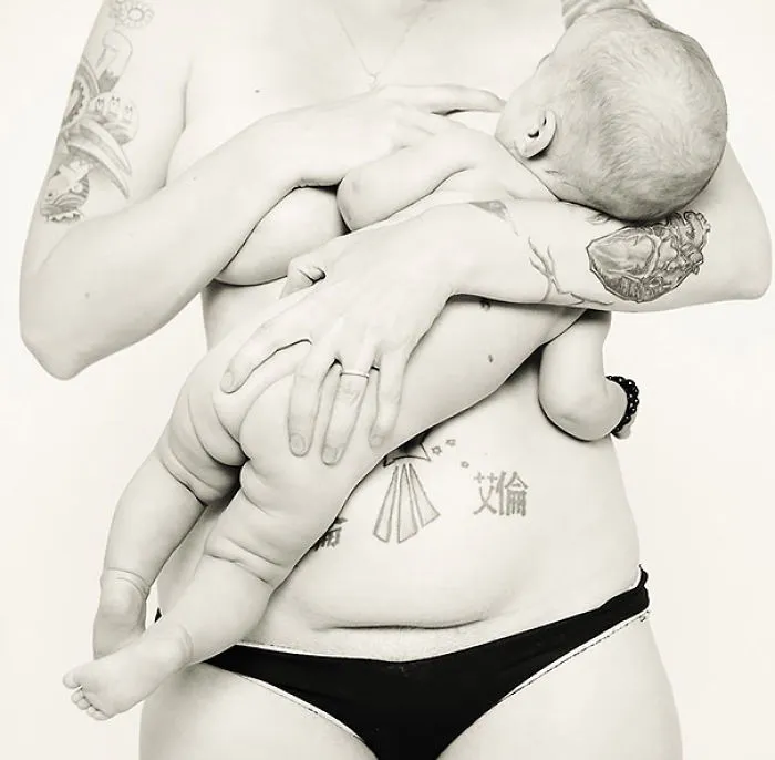 Tattooed parent holds a baby close, showcasing their body art.