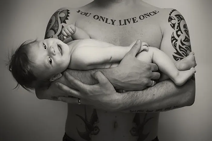 Tattooed parent holding a smiling baby, showcasing beautiful bond and inked art together.