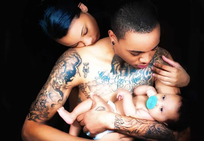 Tattooed parents lovingly holding their baby, showcasing beautiful body art and family bond.