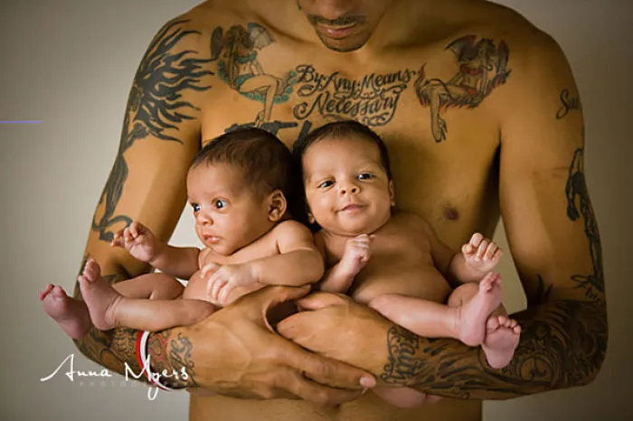 Tattooed parent gently holding twin babies, showcasing family bond and body art.