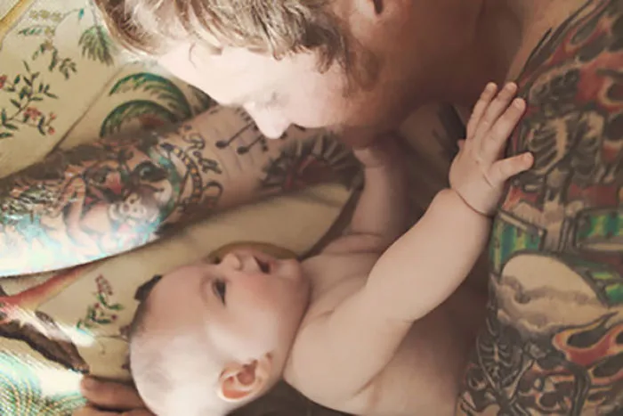 Tattooed parent embracing baby, showcasing beautiful bond and vibrant body art.