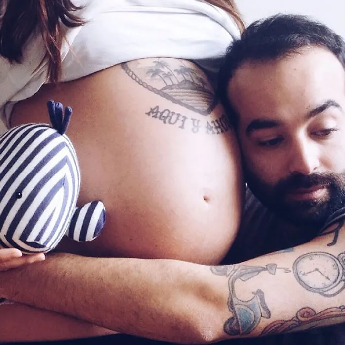 Tattooed parent lovingly embracing pregnant belly, showcasing beautiful bond with baby.