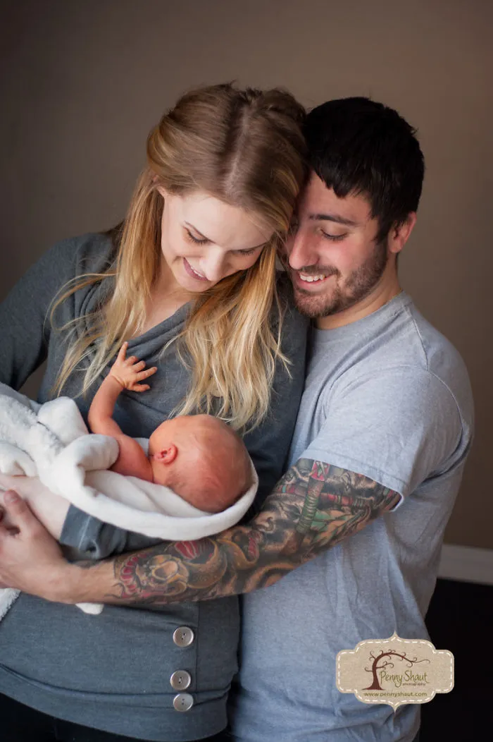 Tattooed parents smiling at their newborn, wrapped in a white blanket, capturing a beautiful family moment.