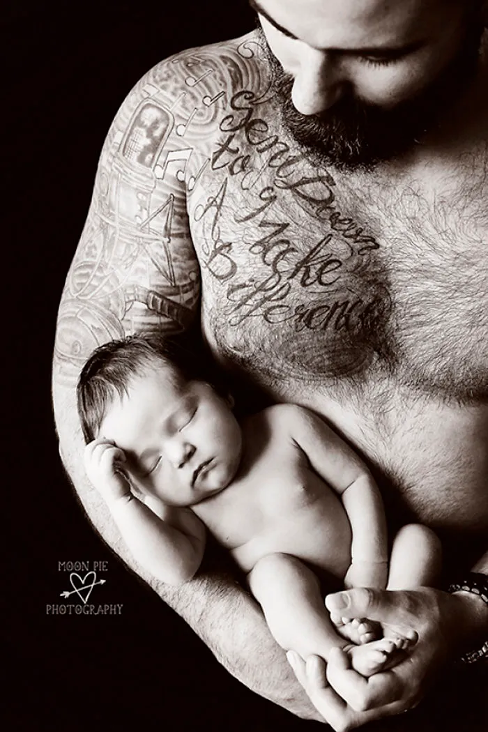 Tattooed parent cradles sleeping baby, displaying tender bond and intricate body art.