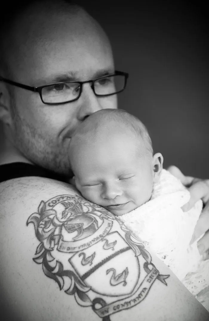 Tattooed parent gently holding smiling baby, showcasing beautiful bond together.