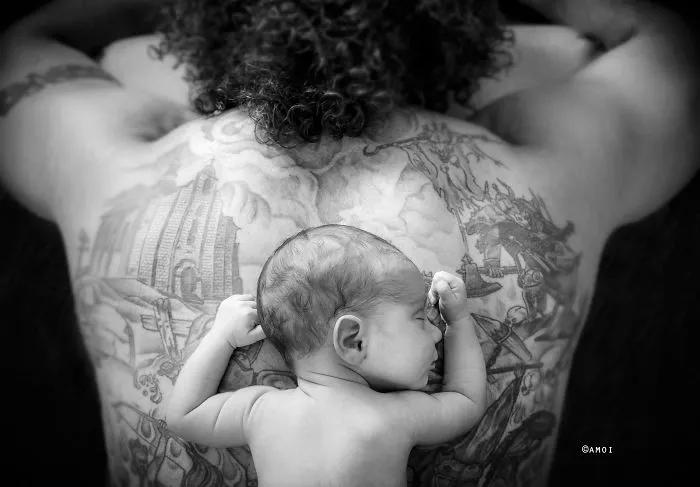 Baby resting on tattooed parent's back, depicting a beautiful connection between babies and their tattooed parents.