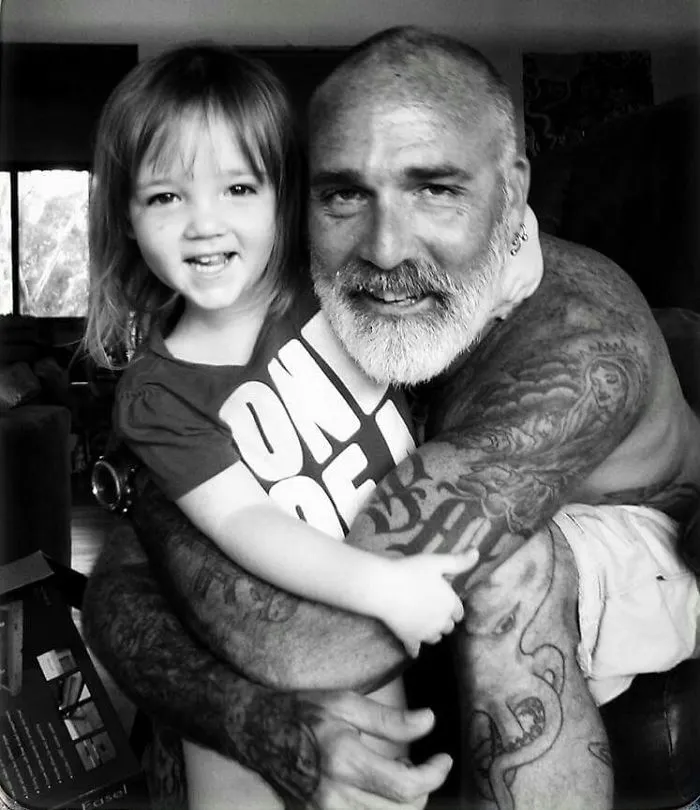 Tattooed parent hugging smiling baby, showcasing beautiful bond.