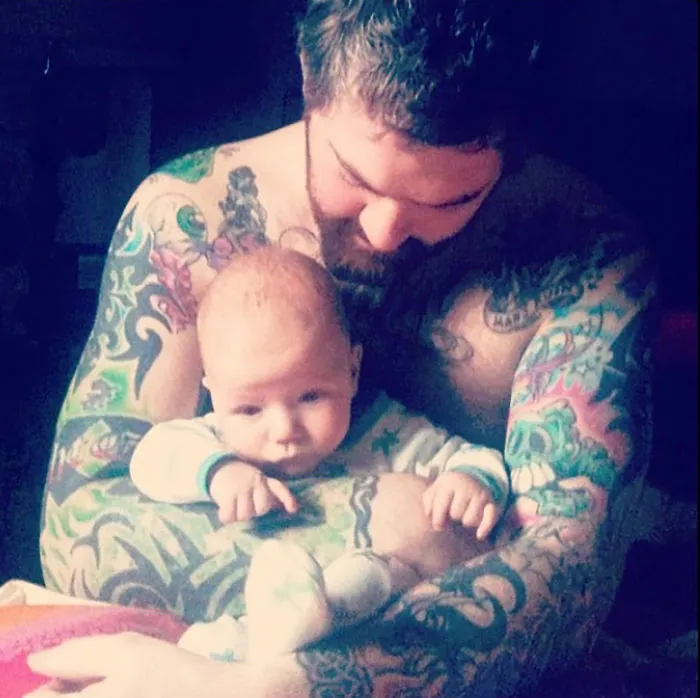 Tattooed parent holding a baby with colorful tattoos visible on their arms, creating a beautiful moment together.