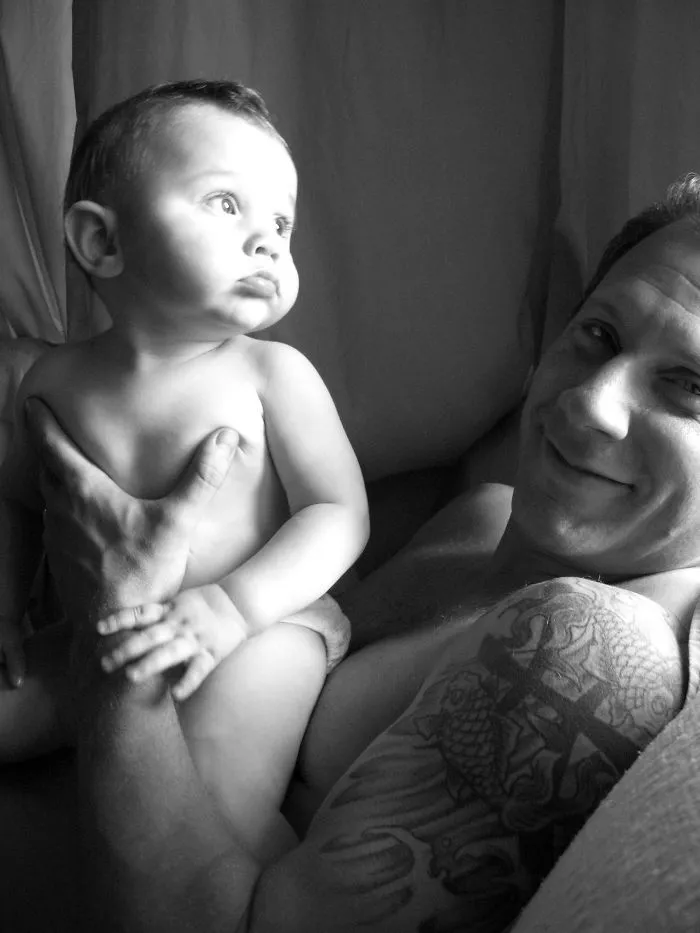 Baby with tattooed parent smiling warmly, showcasing a beautiful bond in black and white.