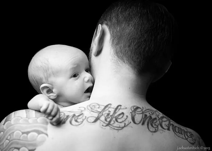 Baby resting on tattooed parent's shoulder, capturing a beautiful bond together.