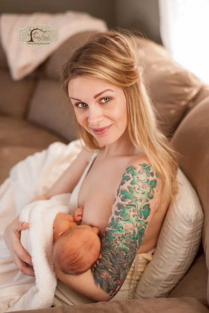 Tattooed parent lovingly holding a baby on a couch, creating a beautiful family moment together.