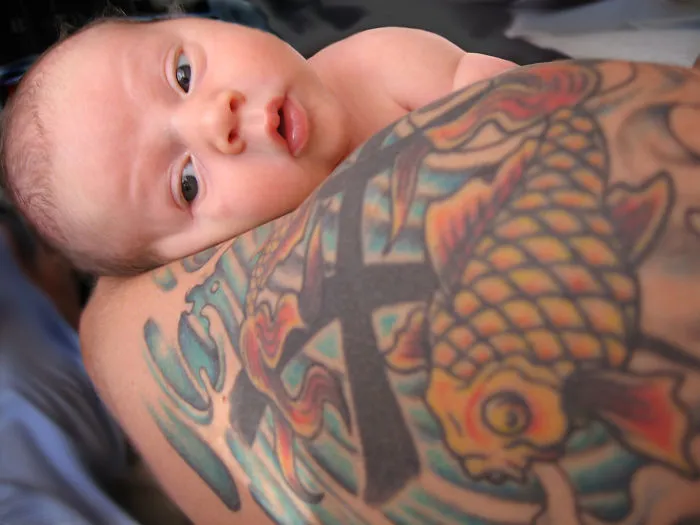 Baby resting on parent's tattooed arm with colorful koi fish design.