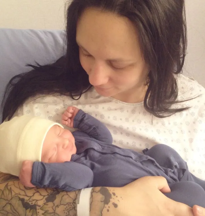 Tattooed parent lovingly holds a newborn baby, highlighting a contrast between ink and innocence.