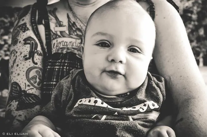 Baby in the arms of a tattooed parent, both looking content and beautiful together.