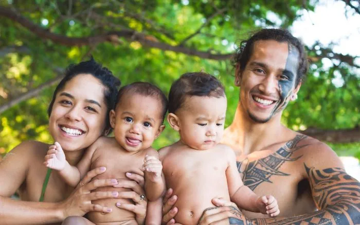 Tattooed parents smiling with their two babies outdoors, showing family beauty and happiness.