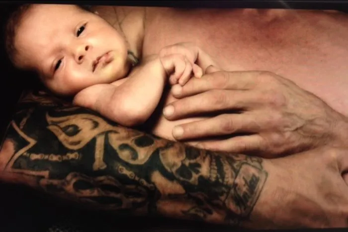 A baby resting on a tattooed parent's arm, showcasing the contrast between soft skin and detailed body art.
