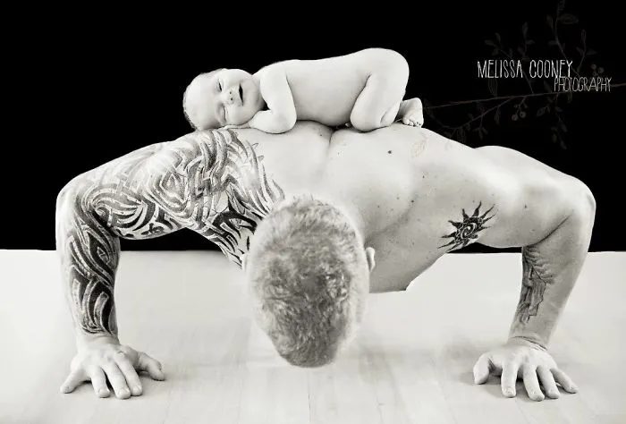 Tattooed parent doing push-up with baby on back, showcasing beautiful bond.