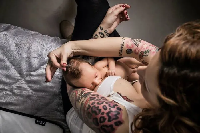 Tattooed parent cradling a sleeping baby, showcasing beautiful inked arms.