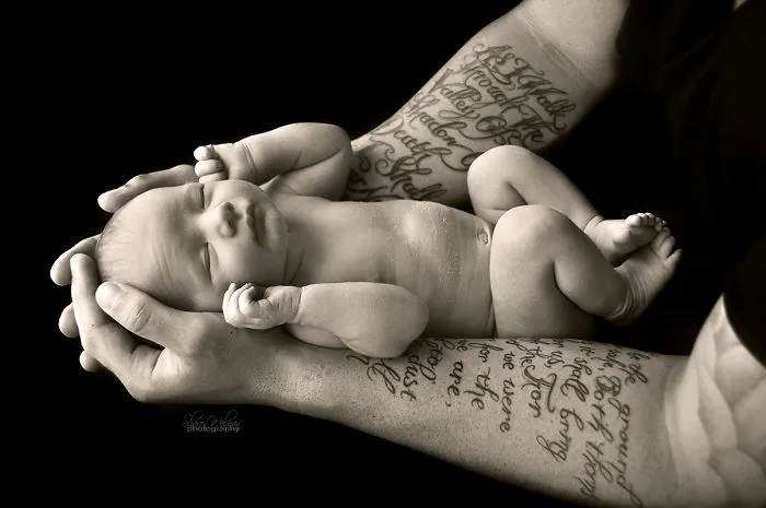 Tattooed parent cradling a newborn baby, showcasing the contrast between ink and innocence.