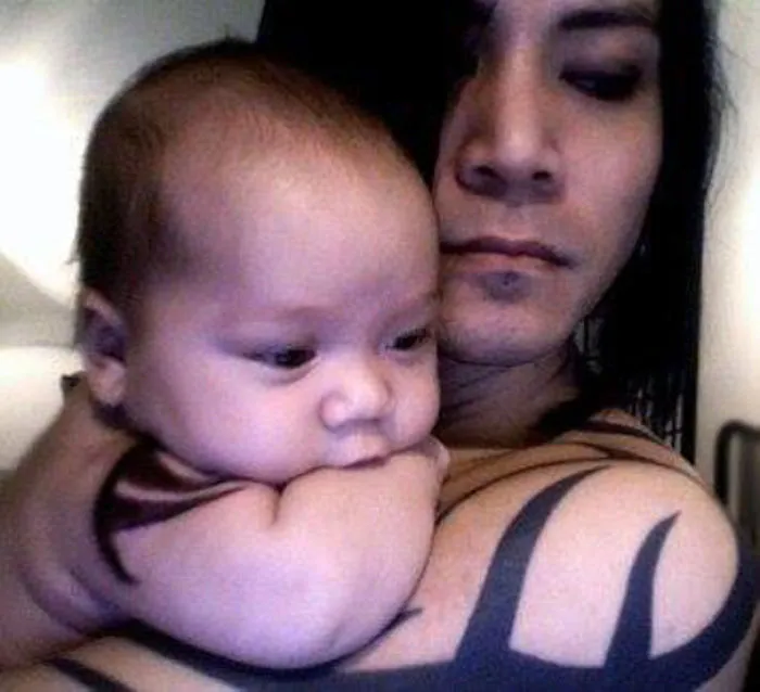 Tattooed parent holding baby, showcasing their beautiful bond together.