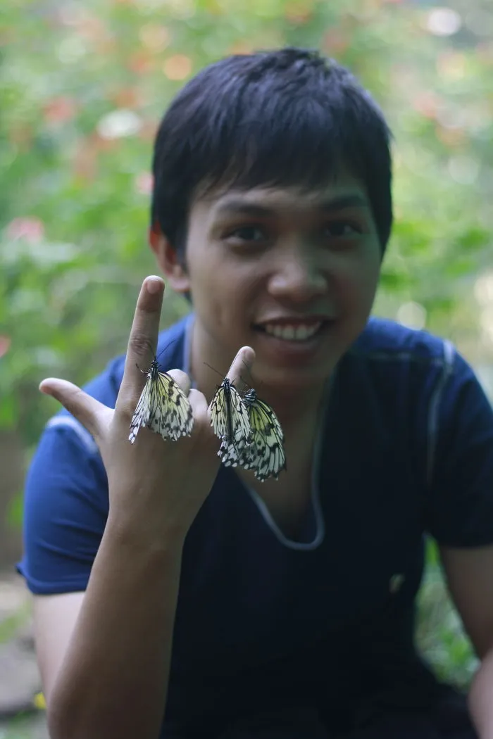 Young man with butterflies on fingers showing animals with butterflies in a natural garden setting.