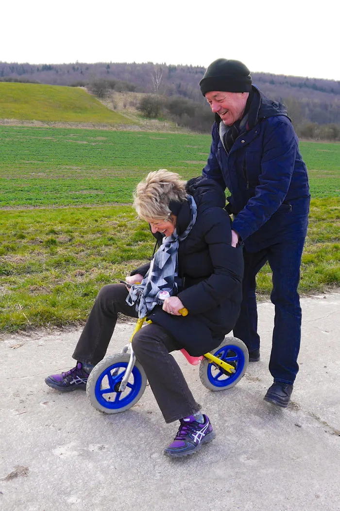 Elderly couple having fun with woman on a small tricycle, smiling outdoors.