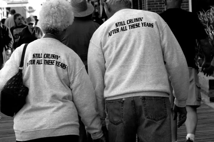 Elderly couple walking together, wearing matching shirts that say "Still Cruisin' After All These Years."
