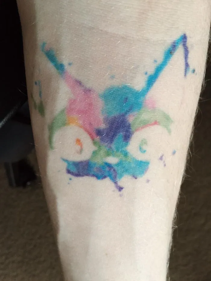 Colorful watercolor style simple cat tattoo on forearm.