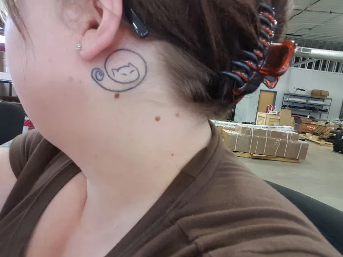 Line art cat tattoo design behind a woman's ear.