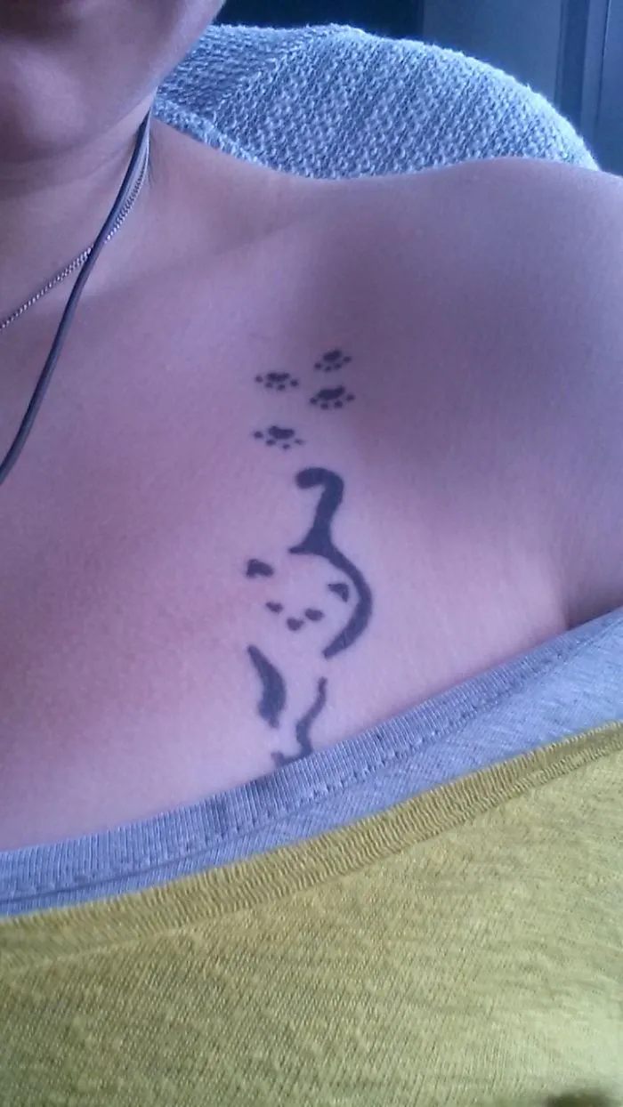 Simple cat tattoo design on shoulder with paw prints, featuring clean line art.