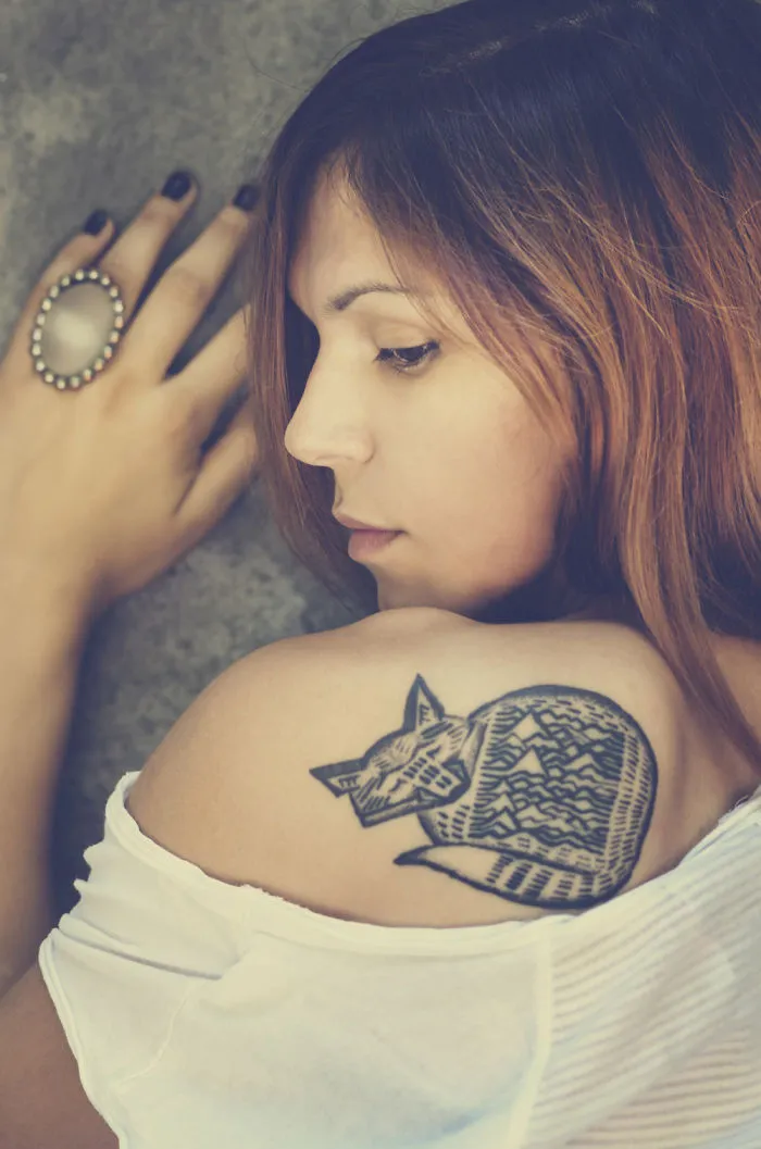 Woman with simple cat tattoo design on shoulder, showcasing line art style.