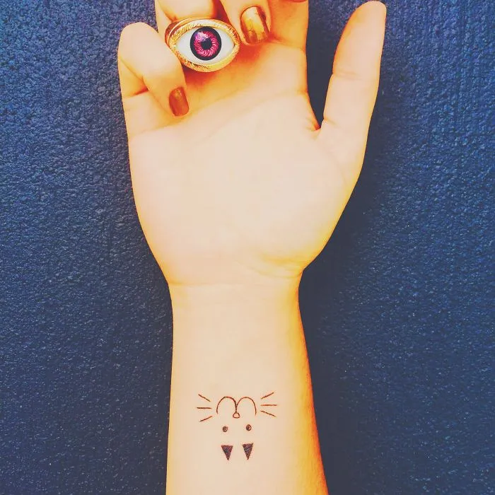 Minimalist cat tattoo design on forearm with an eye-shaped ring, perfect for cat lovers and line art enthusiasts.