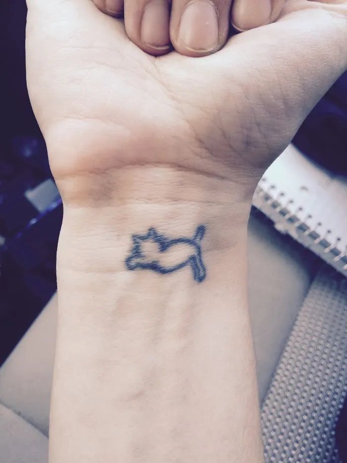 Simple cat tattoo design in line art on a person's wrist.