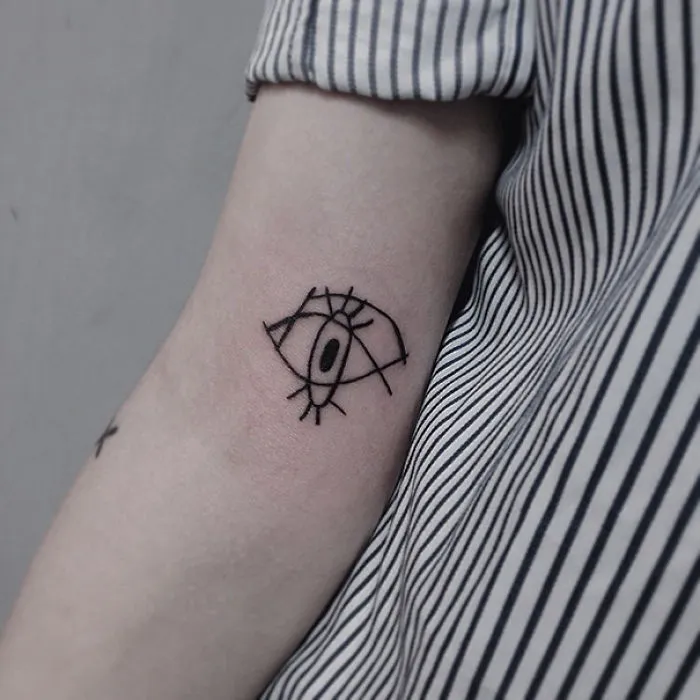 Picasso-inspired eye tattoo on forearm, person wearing a striped shirt.