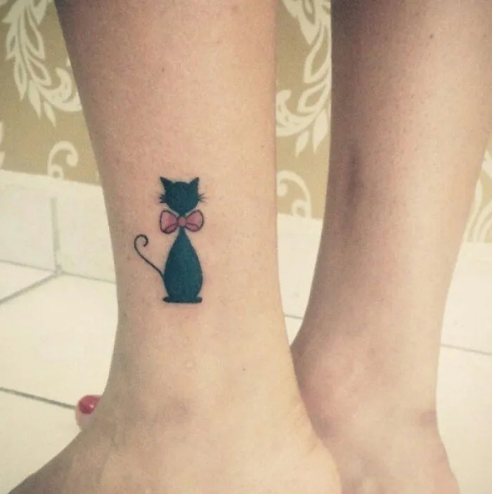 Line art cat tattoo design featuring a black cat with a pink bow on an ankle.