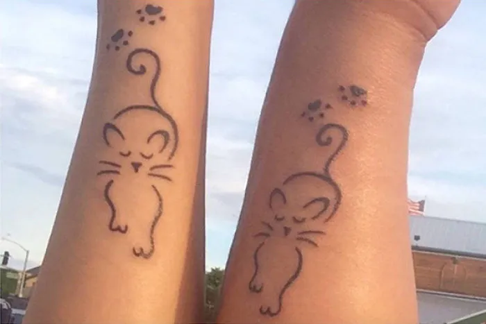 Simple cat tattoo designs on arms, featuring line art with paw prints.