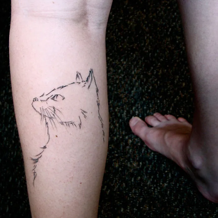 Line art cat tattoo on a person's leg, showcasing a simple design for cat lovers.