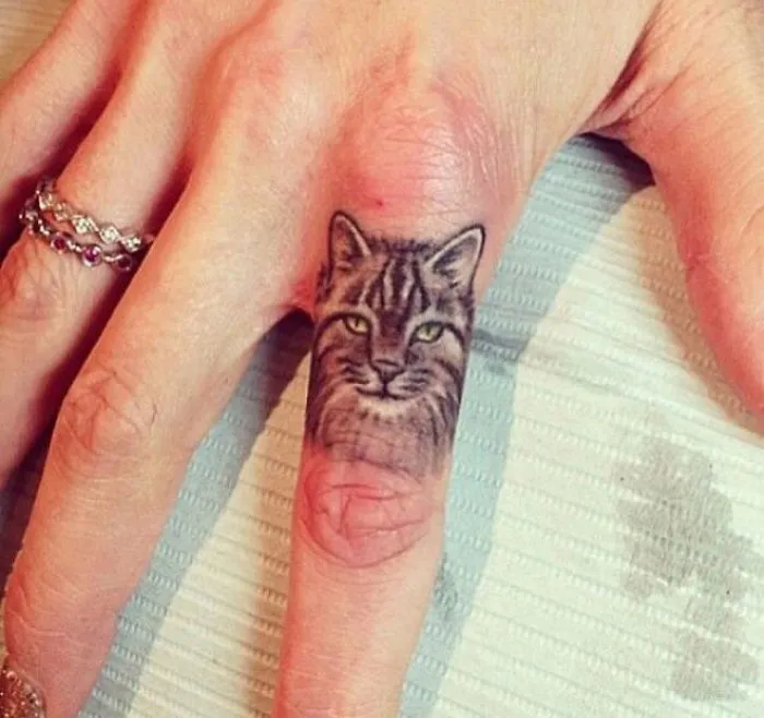 Simple cat tattoo design on a finger, showcasing line art details, perfect for cat lovers.