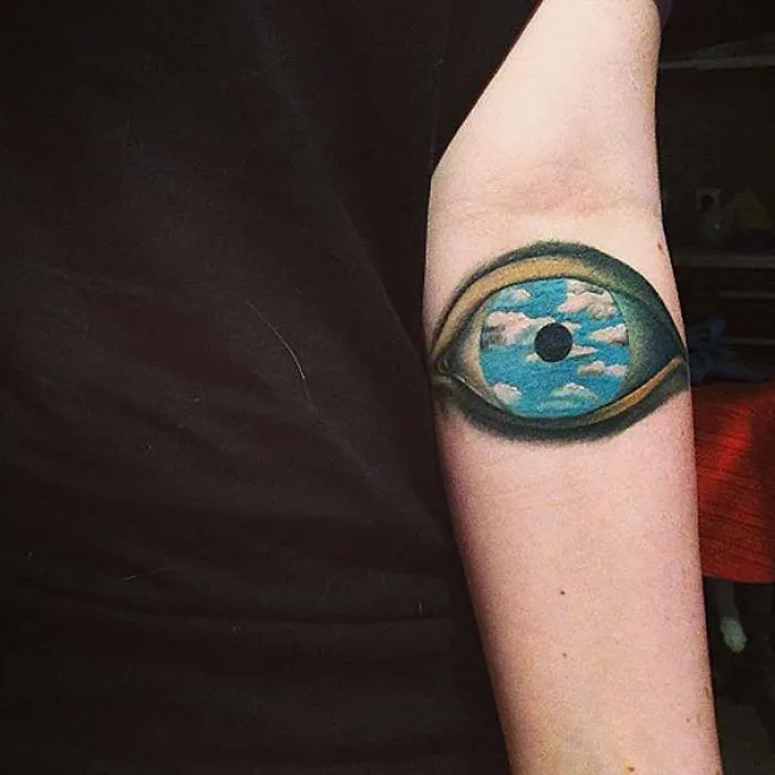 Picasso-inspired tattoo of an eye with a sky and clouds design on a person's arm.