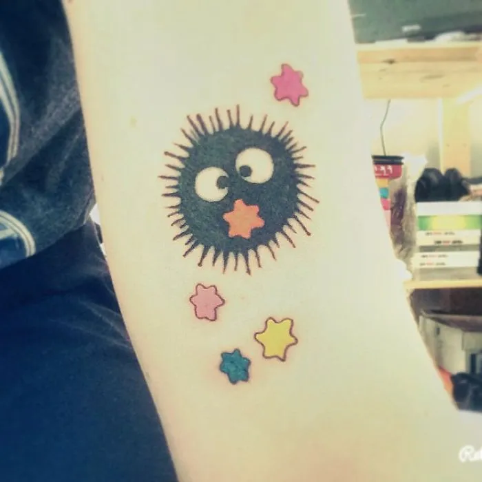 Studio Ghibli tattoo featuring a soot sprite and colorful stars inspired by Miyazaki films on an arm.