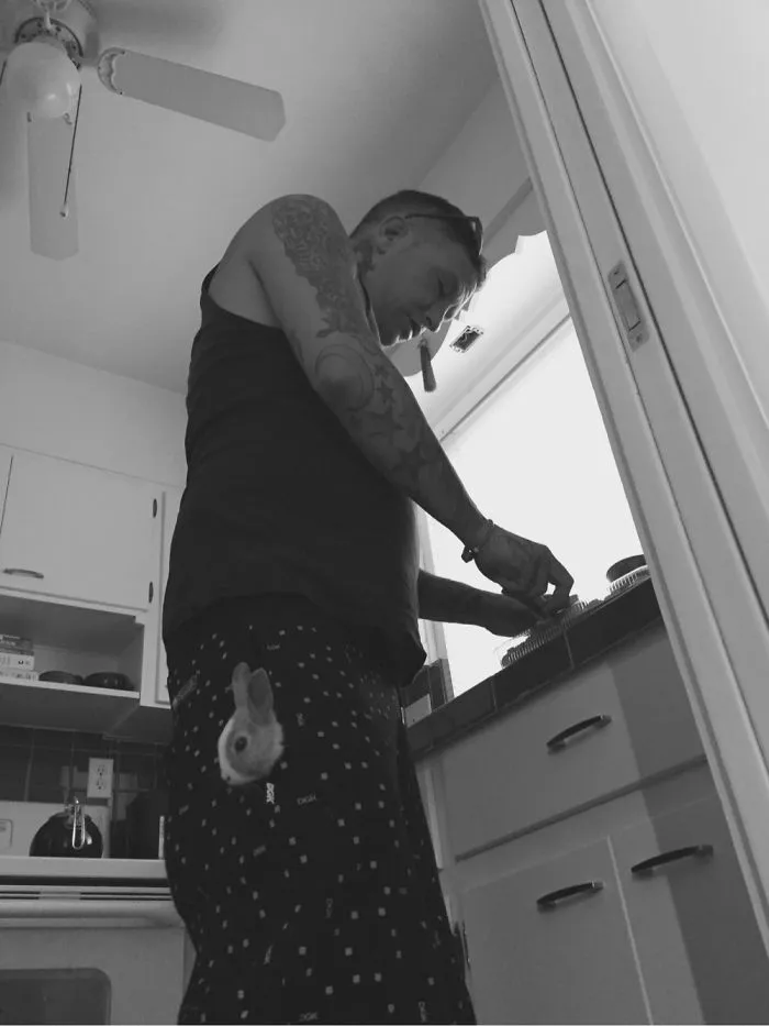 Man in a kitchen with tattoos wearing pants featuring a cute bunny design on the pocket.