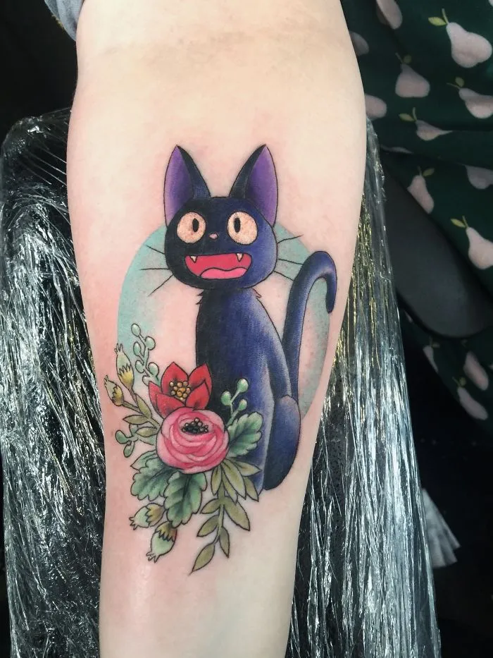 Studio Ghibli tattoo featuring a black cat with colorful flowers, inspired by Miyazaki films.