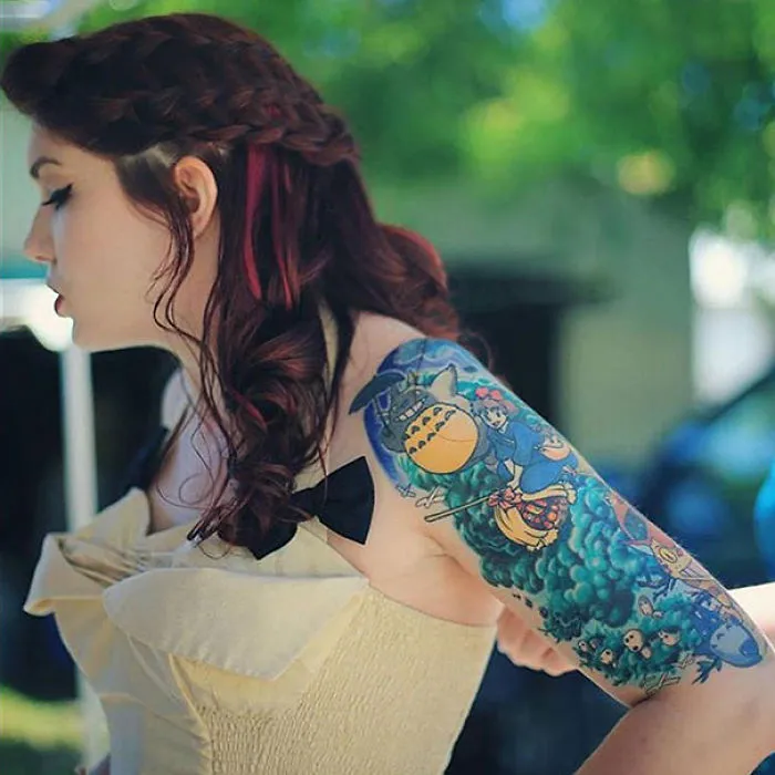 Woman with Studio Ghibli tattoo sleeve inspired by Miyazaki films, featuring vibrant colors and iconic characters.