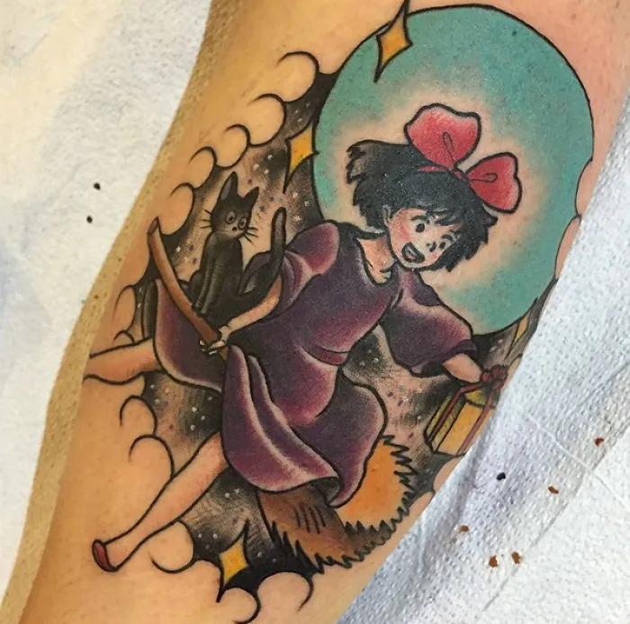 Studio Ghibli tattoo of a girl with a red bow and black cat on a broom, inspired by Miyazaki films.