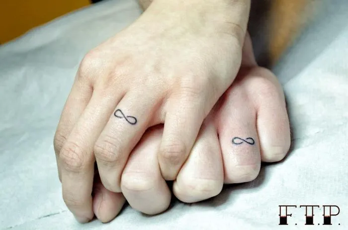 Couple with matching wedding tattoos as infinity symbols on their fingers.